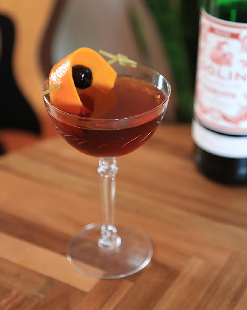 An example of the Bourbon Manhattan, the mixed drink (drink) featuring bourbon whiskey, Dolin Rouge Vermouth de Chambéry, Angostura bitters, orange twist, and maraschino cherry; photo by Megan Heinowski