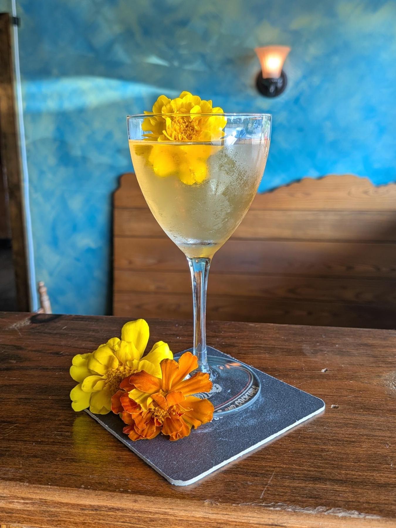 An example of the Hay Fever, the mixed drink (drink), by Cara Grey, Austin, TX, featuring Hayman’s Old Tom Gin, Cocchi Americano Bianco, Alpeggio Hay Liqueur, grapefruit bitters, and flower; photo by Cara Grey