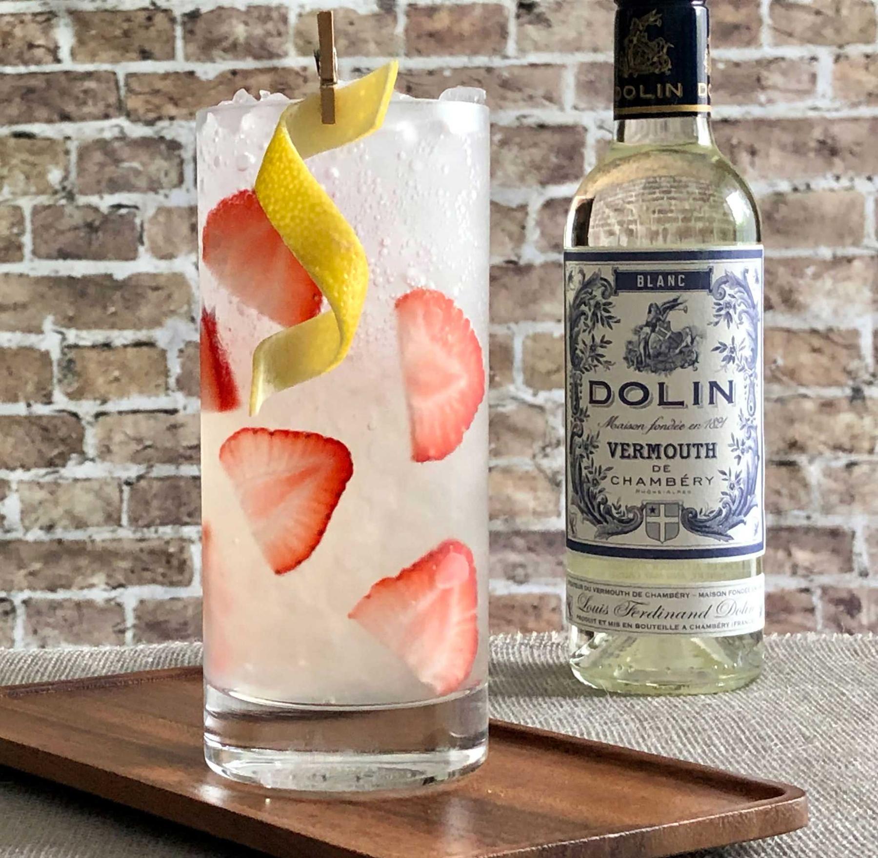 An example of the First Test Sling, the mixed drink (drink) featuring soda water, blanco tequila, Dolin Blanc Vermouth de Chambéry, lemon juice, simple syrup, lemon twist, and strawberry; photo by Lee Edwards