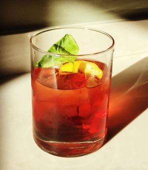 An example of the Plum Negroni, the mixed drink (drink), by Michael Schall, Bar Camillo, Brooklyn, featuring Averell Damson Plum Gin Liqueur, Mattei Cap Corse Blanc Quinquina, Comoz Blanc Vermouth de Chambèry, and basil leaf
