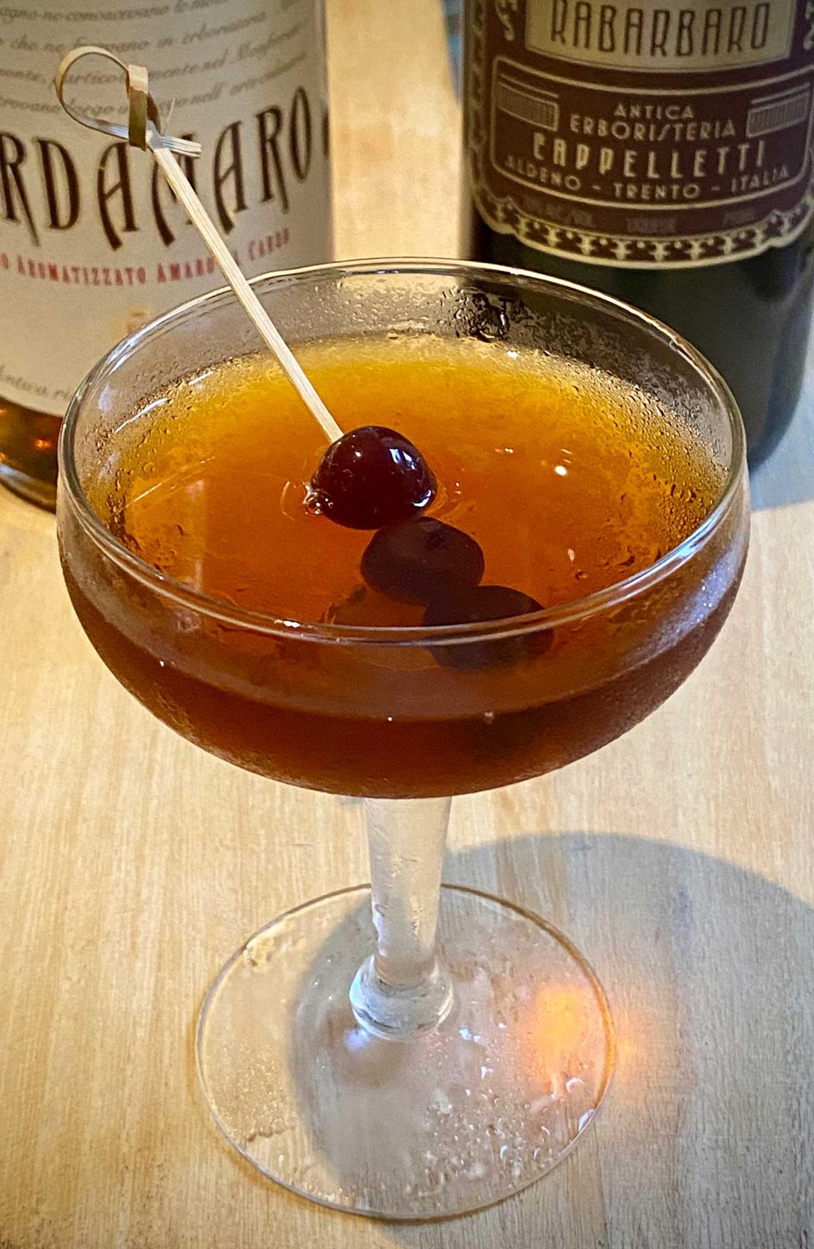 An example of the Amaro Manhattan, the mixed drink (drink) featuring bourbon whiskey, Cardamaro Vino Amaro, Amaro Sfumato Rabarbaro, and maraschino cherry; photo by Martin Doudoroff