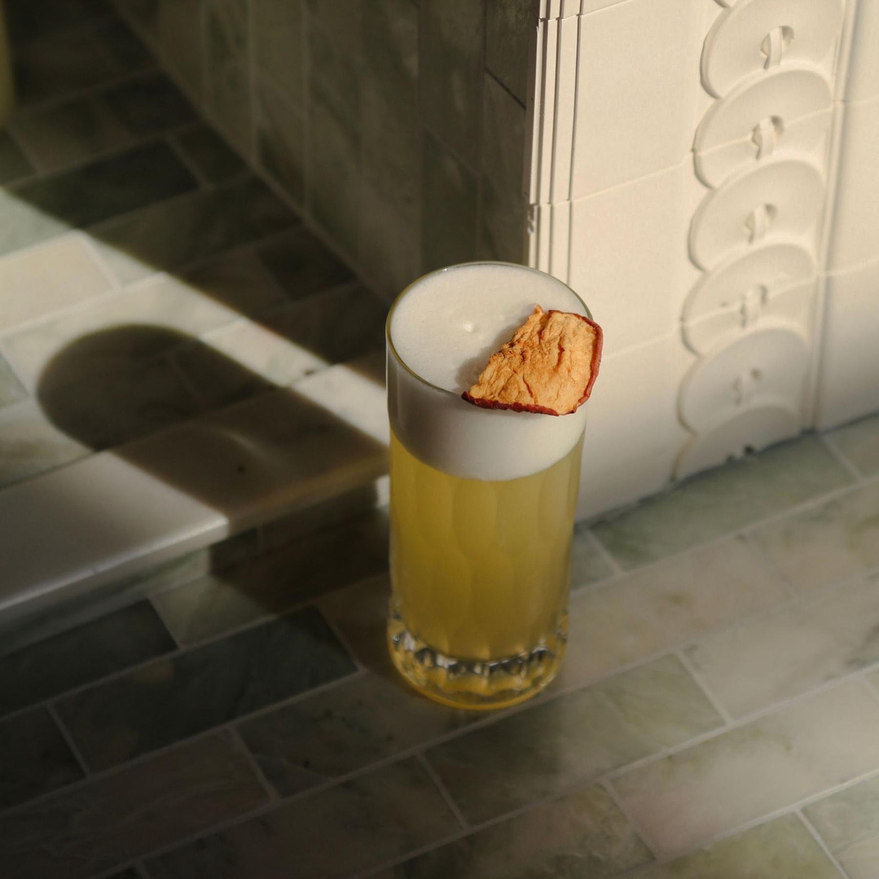 An example of the The Delicious Sour, the mixed drink (drink), adapted from The Flowing Bowl, by William Schmidt, featuring calvados, Rothman & Winter Orchard Peach Liqueur, egg white, lemon juice, soda water, rich simple syrup, apple slice, and peach slice; photo by Megan Heinowski