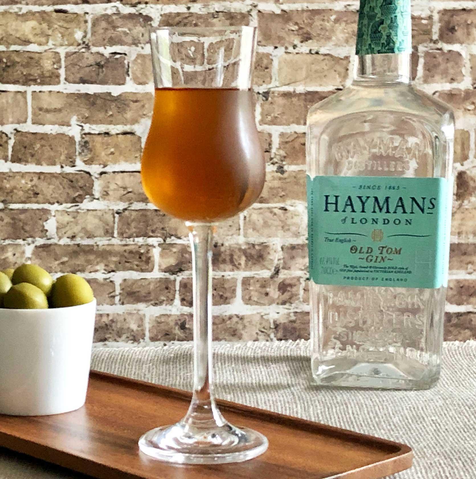 An example of the The Spring Cocktail, the mixed drink (drink), adapted from the Savoy Cocktail Book by Erik Ellestad, featuring Hayman’s Old Tom Gin, Bonal Gentiane-Quina, Bénédictine, orange bitters, and olive; photo by Lee Edwards
