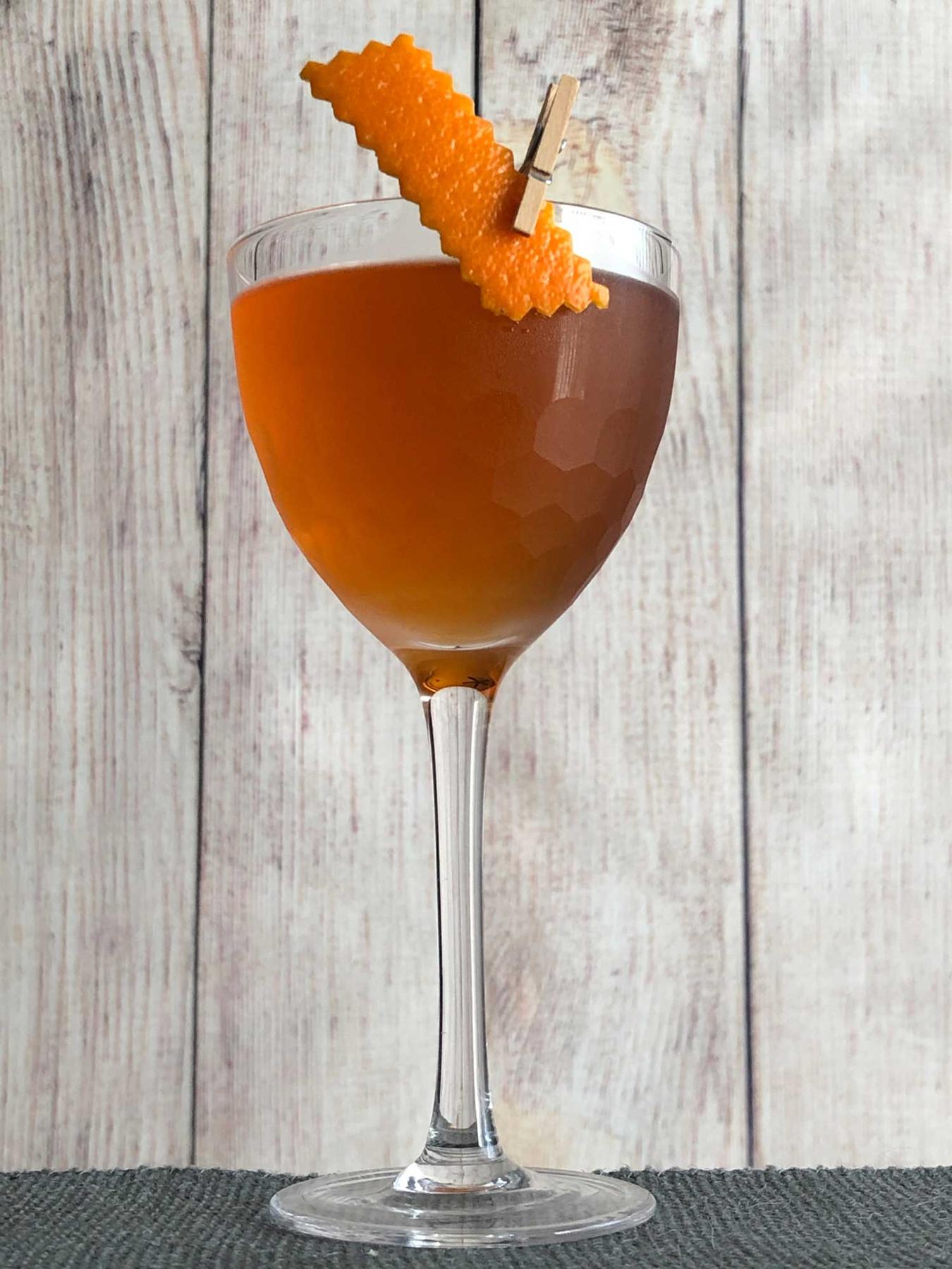 An example of the Overtime Cocktail, the mixed drink (drink), by based on the Coin Toss, Death & Co, New York City, featuring The Scarlet Ibis Trinidad Rum, Cocchi Vermouth di Torino ‘Storico’, Dolin Génépy le Chamois Liqueur, Bénédictine, Peychaud’s Aromatic Cocktail Bitters, and orange twist; photo by Lee Edwards