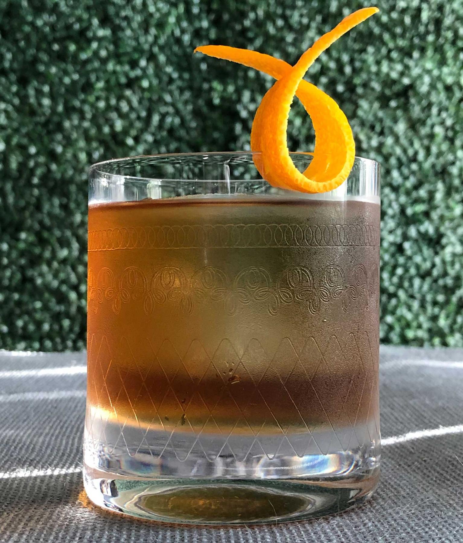 An example of the Piston Honda, the mixed drink (drink), by Brandon Wise, Sage Restaurant Group, featuring japanese whisky, Bonal Gentiane-Quina, maraschino liqueur, orange bitters, large ice cube, and orange twist; photo by Lee Edwards