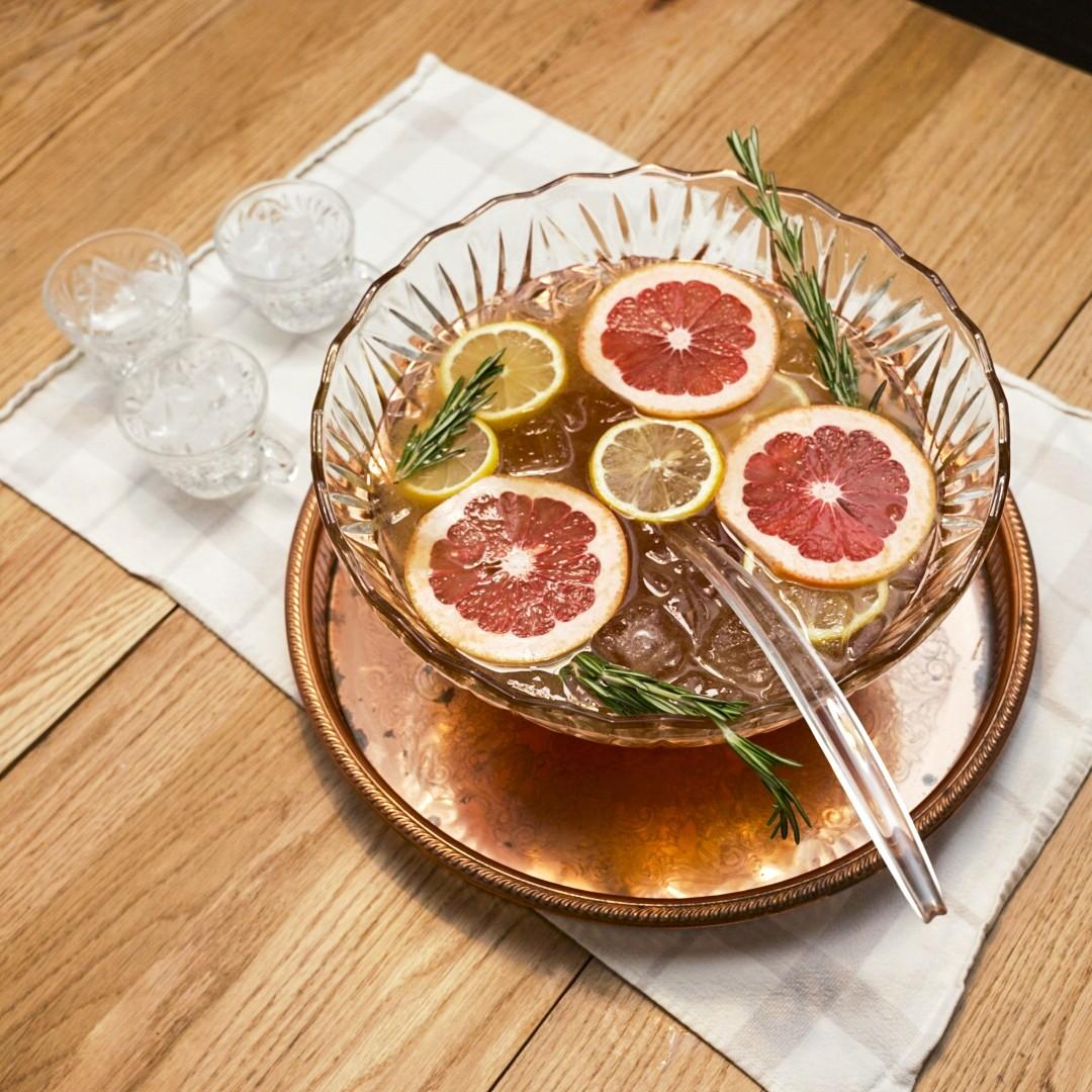 An example of the Orchard Punch, the mixed drink (batch), by Kellie Thorn, featuring Hayman’s London Dry Gin, Henriques & Henriques Rainwater Madeira, pear cider, lemon juice, lemon oleo-saccharum, block of ice, fresh fruit, and sprig of rosemary; photo by Madison Young