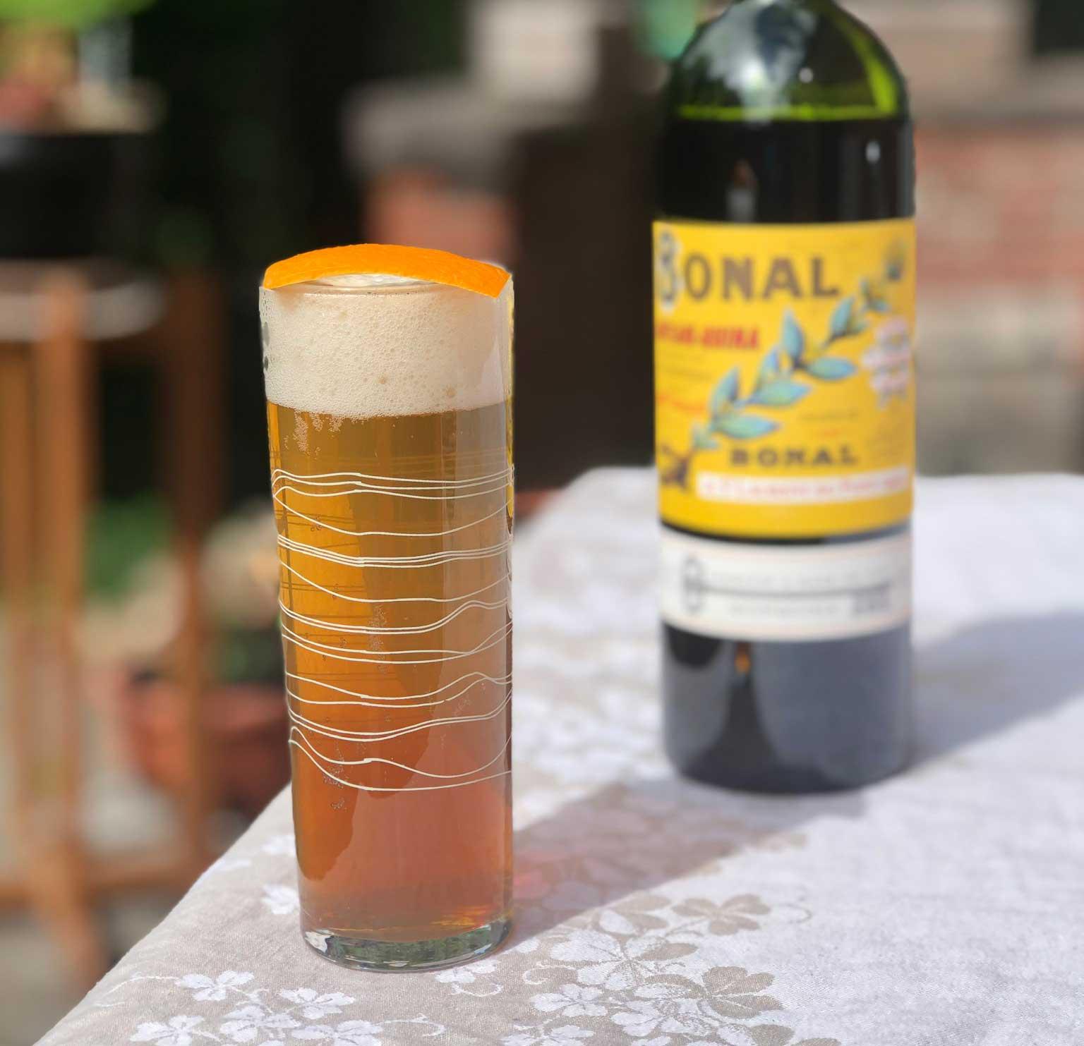 An example of the Amer Frontière, the mixed drink (drink) featuring lager, Bonal Gentiane-Quina, orange bitters, and orange twist