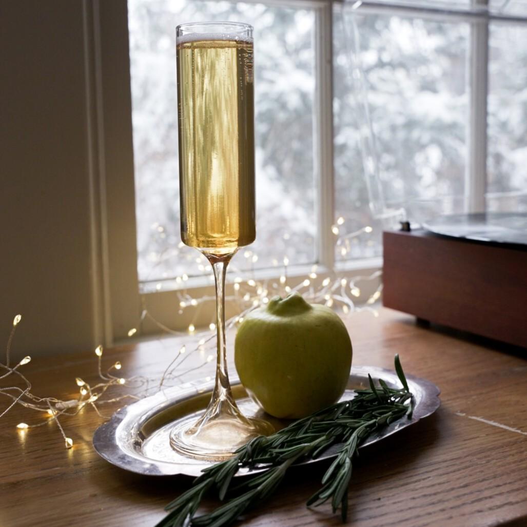 An example of the Quincess, the mixed drink (drink), Adapted from a recipe by Zach Painter, TX, featuring Rothman & Winter Orchard Quince Liqueur, sparkling wine, Dolin Dry Vermouth de Chambéry, orange bitters, and sprig of rosemary; photo by Madison Young