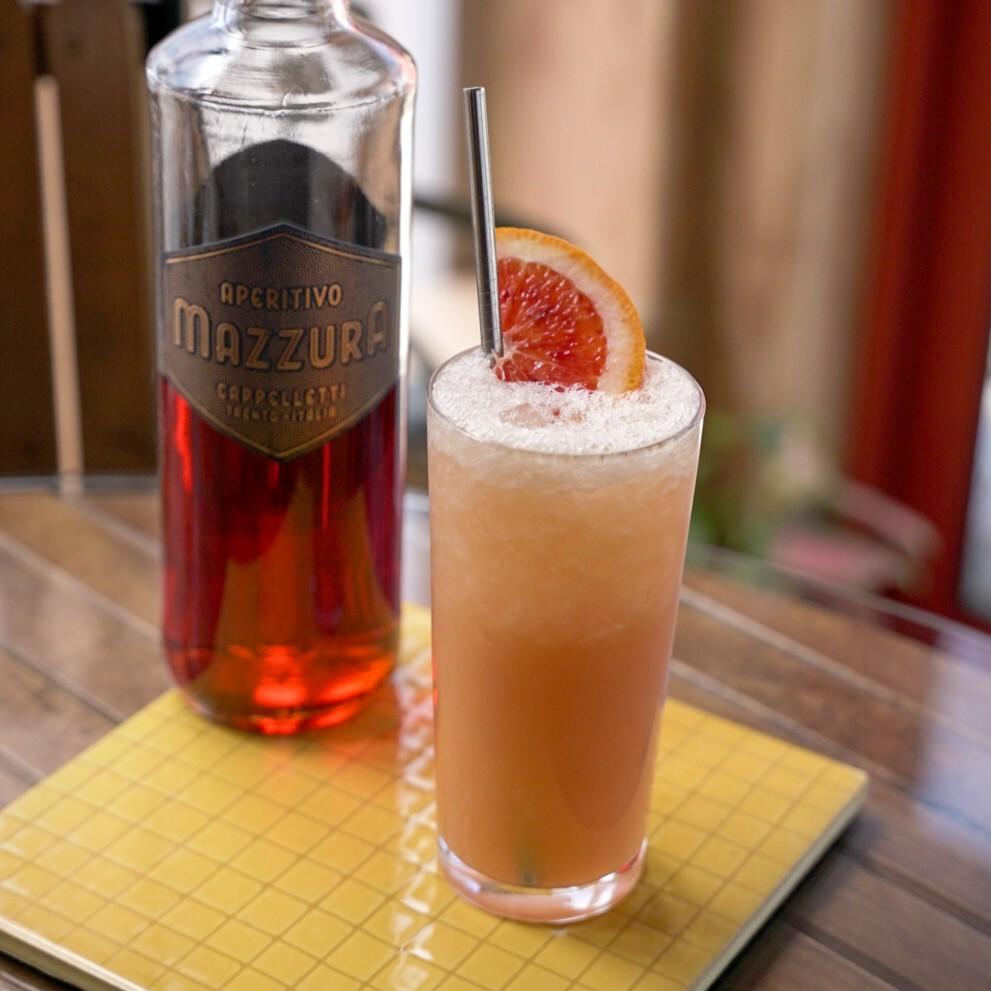 An example of the The Maddalena #2, the mixed drink (drink) featuring orange juice, Aperitivo Mazzura, and orange wedge; photo by Madison Young