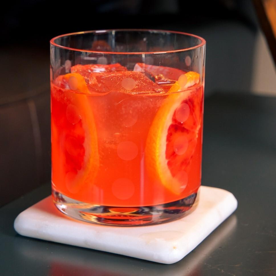 An example of the Tarocco Spritz, the mixed drink (drink), by Baiocchi & Pariseau, featuring prosecco, Hayman’s London Dry Gin, blood orange juice, Aperitivo Cappelletti, lemon juice, vanilla syrup, and blood orange wheel