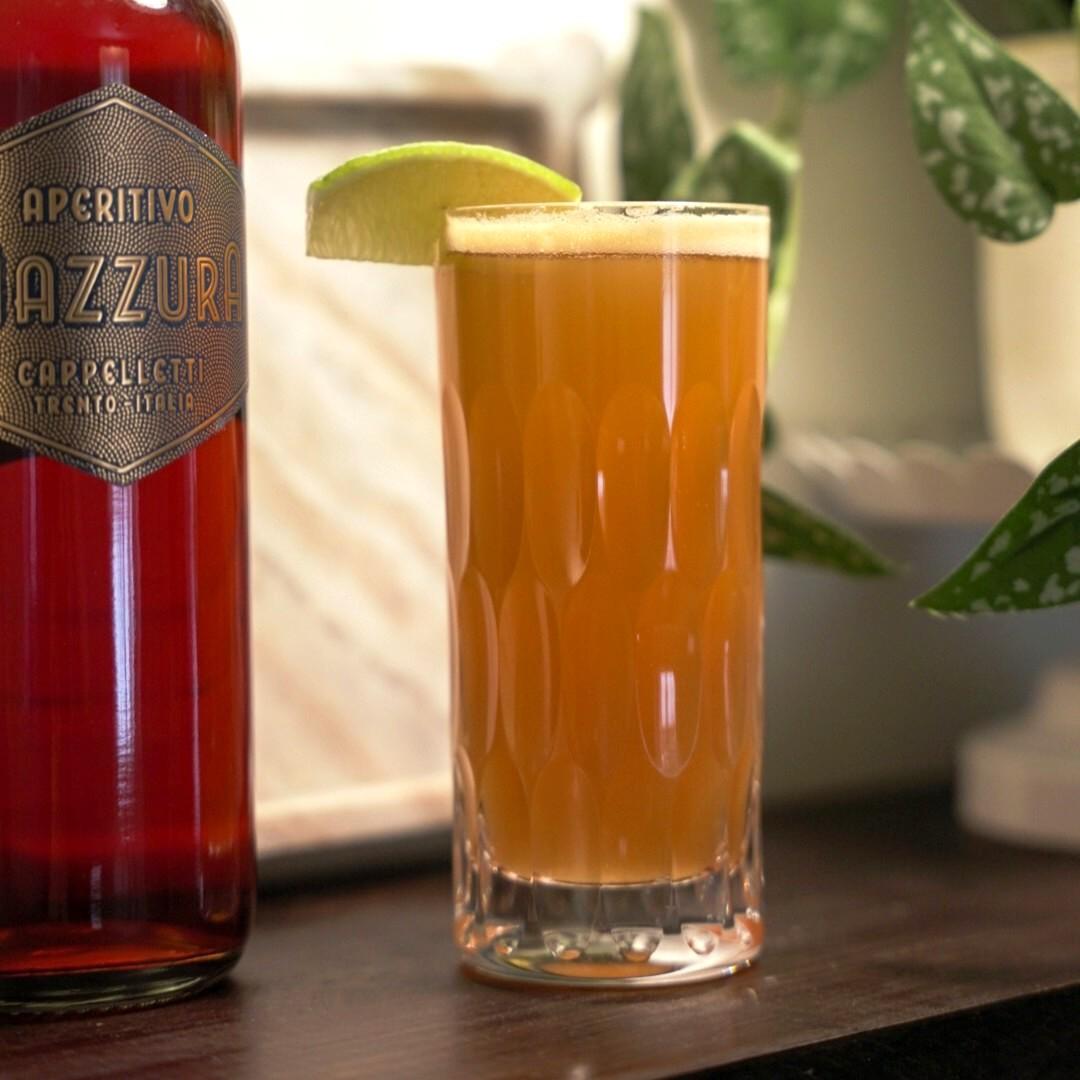 An example of the Day Trip, the mixed drink (drink), by Natasha David, featuring white beer, Aperitivo Mazzura, lime juice, pineapple syrup, passion fruit liqueur, and lime wedge; photo by Madison Young